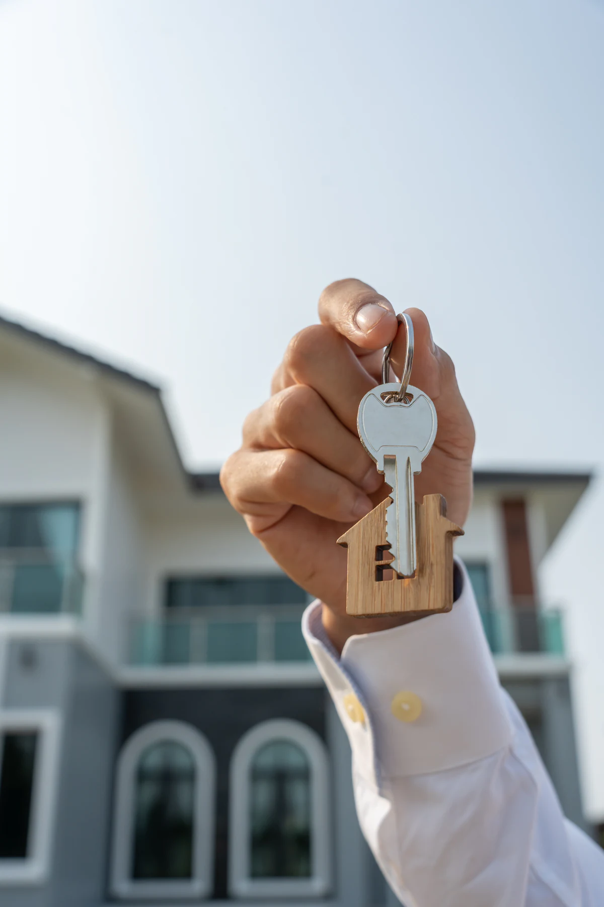 Immobilienmakler hält einen Hausschlüssel vor einer Immobilie