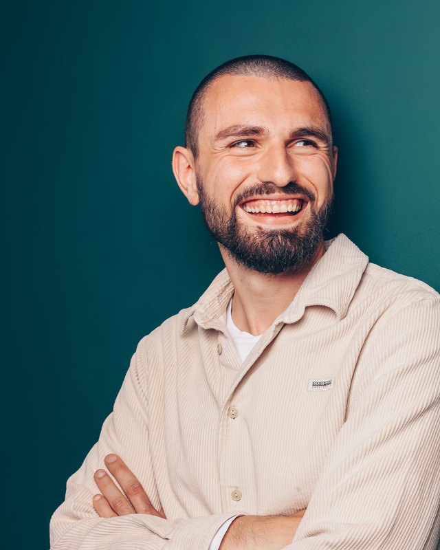 Christos Papageorgiou – dein persönlicher Ansprechpartner bei Sichtio Christos Papageorgiou mit verschränkten Armen vor petrolfarbenem Hintergrund